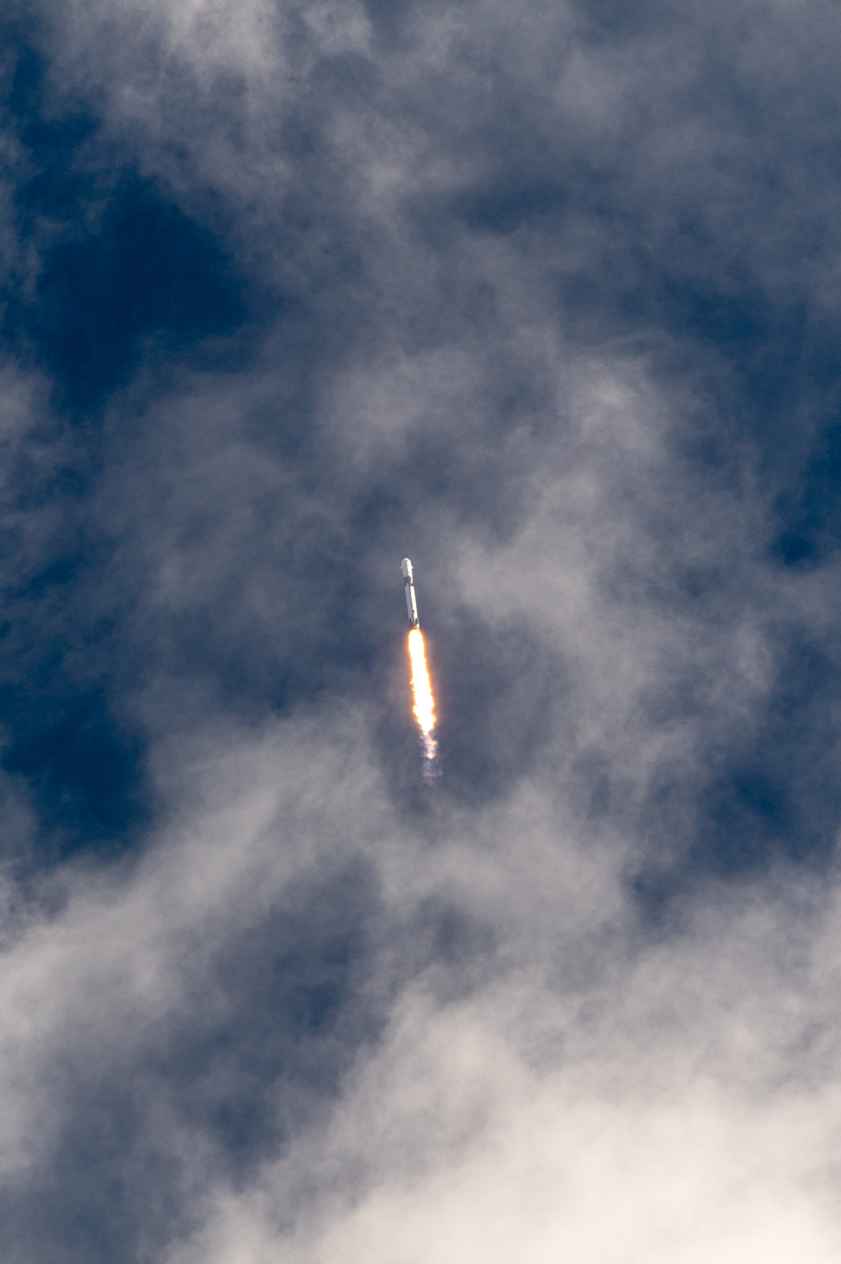 Falcon 9 on its trajectory towards orbit with some light clouds.