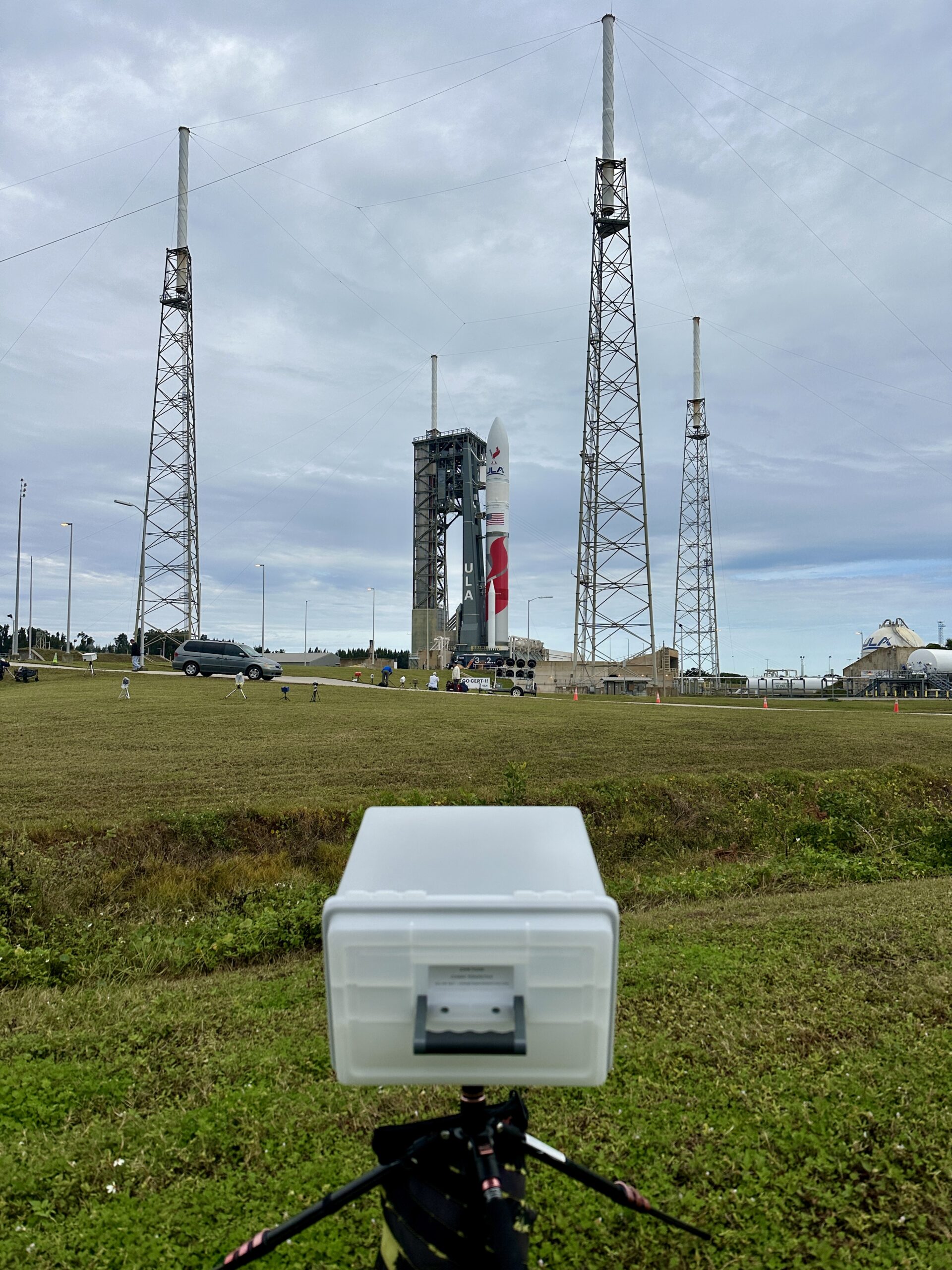 A white box on a tripod containing a Nikon DSLR is setup pointed towards the rocket at SLC-41.